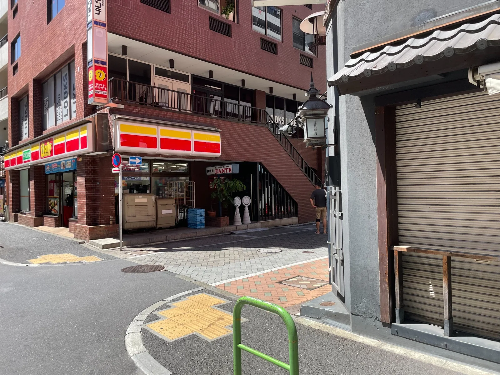 赤いレンガ調の建物の角。1階に「デイリーヤマザキ」、外側に上階へ続く階段