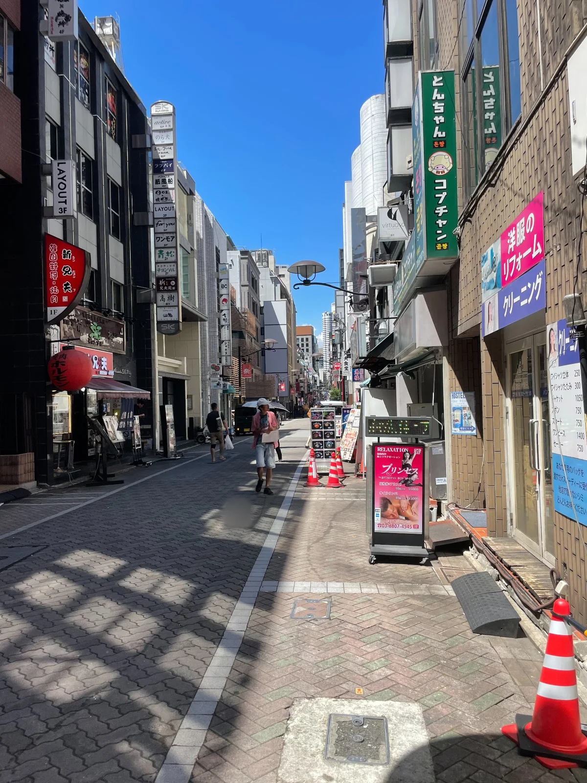 両側に袖看板が並ぶ石畳の通り。奥に歩行者と街路灯