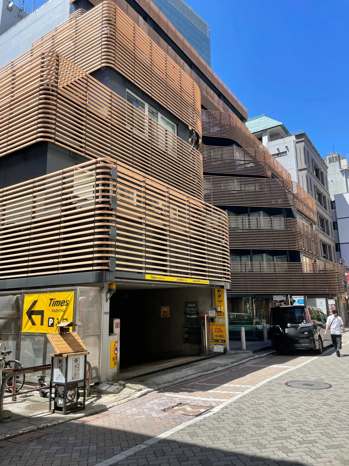木のルーバーで覆われた外装の建物。1階に「Times PARKING」の黄色い看板と駐車場入口